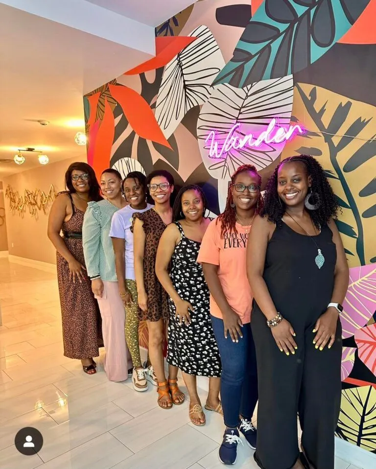A group of women smiling in front of the signature pink neon Wander sign during a group getaway stay at Wanderstay Boutique Hotel, an excellent adult-only hotel Houston option for bachelorette parties.