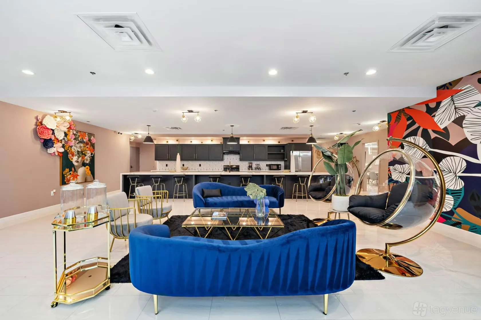 A modern lobby with a blue velvet sofa, gold accents, and a kitchenette.