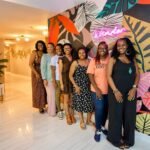 A group of women smiling in front of the signature pink neon Wander sign during a group getaway stay at Wanderstay Boutique Hotel, an excellent adult-only hotel Houston option for bachelorette parties.